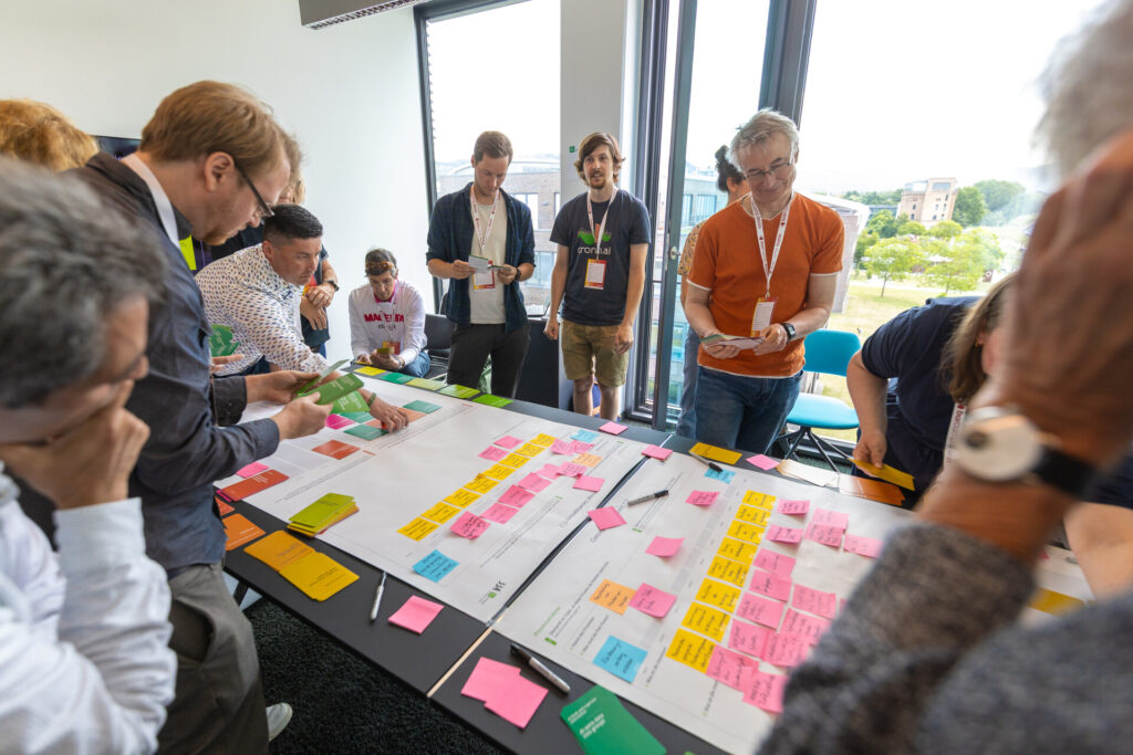 Dokumentation beim Barcamp: Teilnehmende stehen um einen Tisch, auf dem viele Post its kleben.